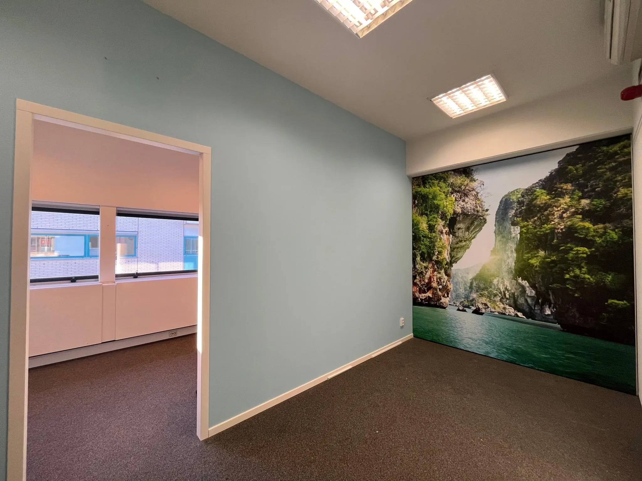 Klein leeg kantoor in Leidse Rijn met een muurposter van een tropisch landschap met rotsen en water.